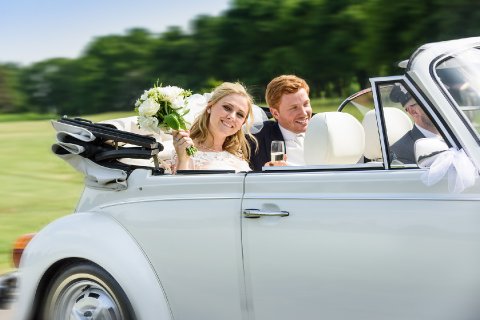 Bride & groom in their wedding car with the bride waving her bouquet. - Jeremy Wilson Photography